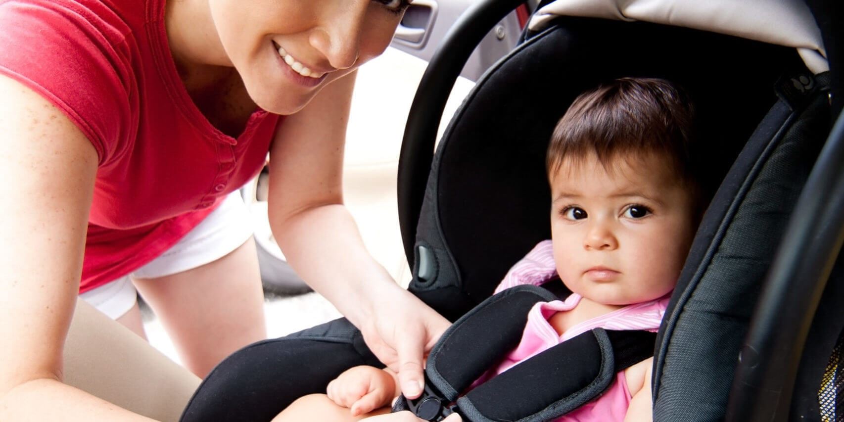 Mother putting her baby in a car seat